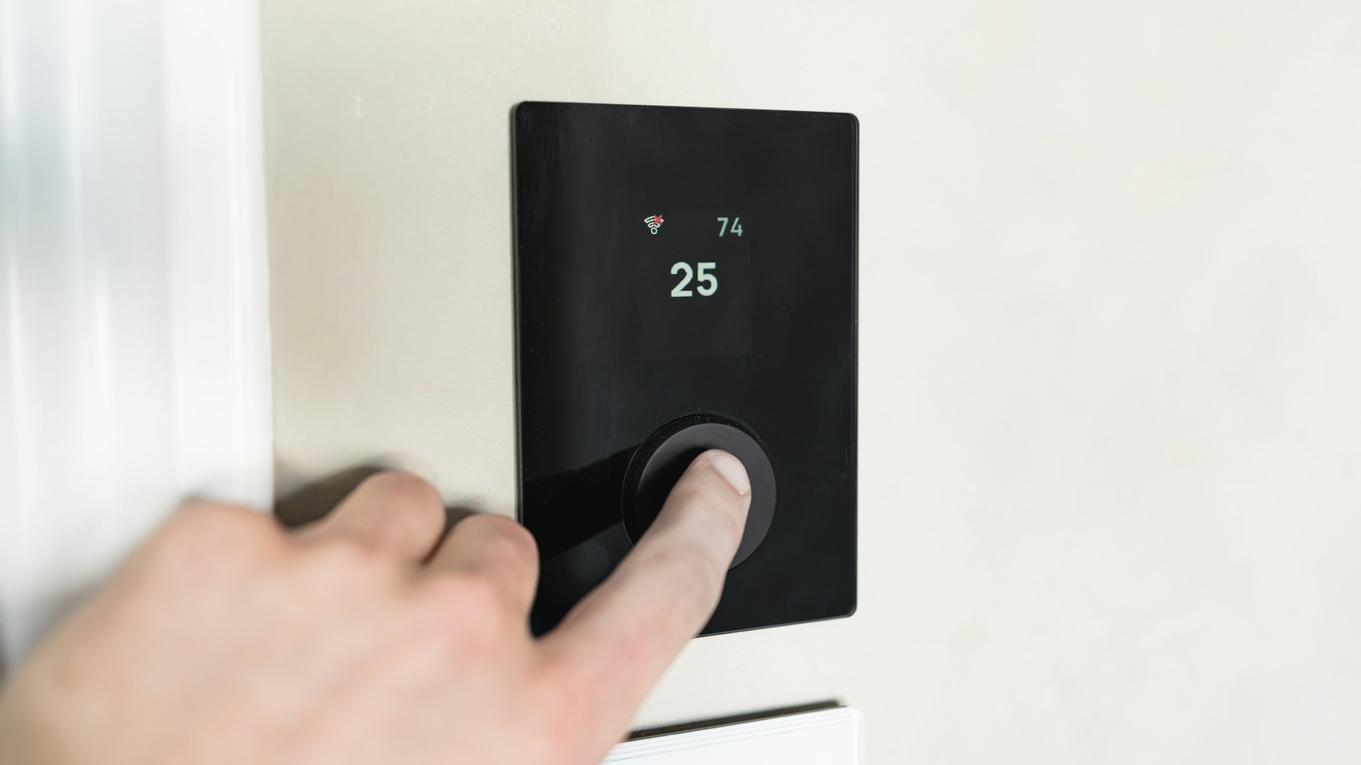 Finger pressing button on digital thermostat display.