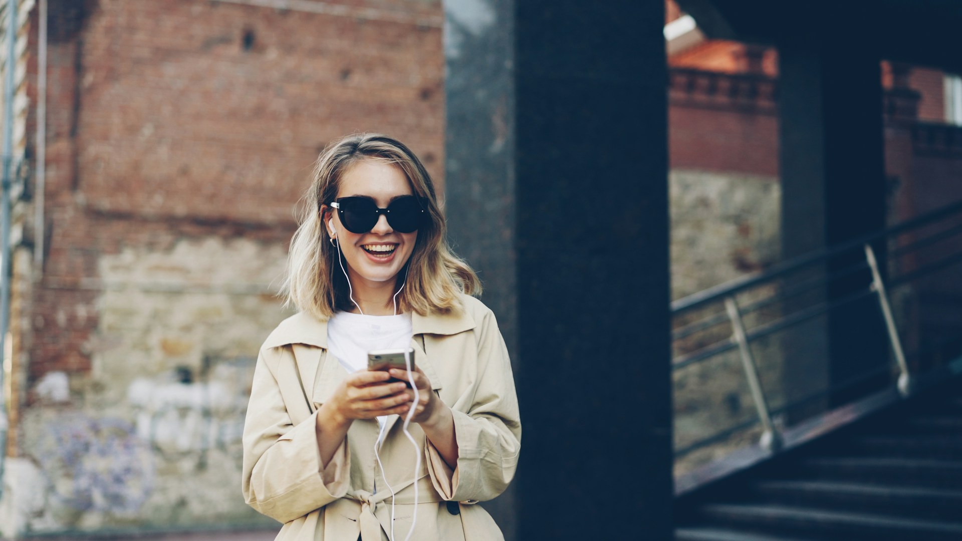 A smiling woman in sunglasses holds a smartphone.