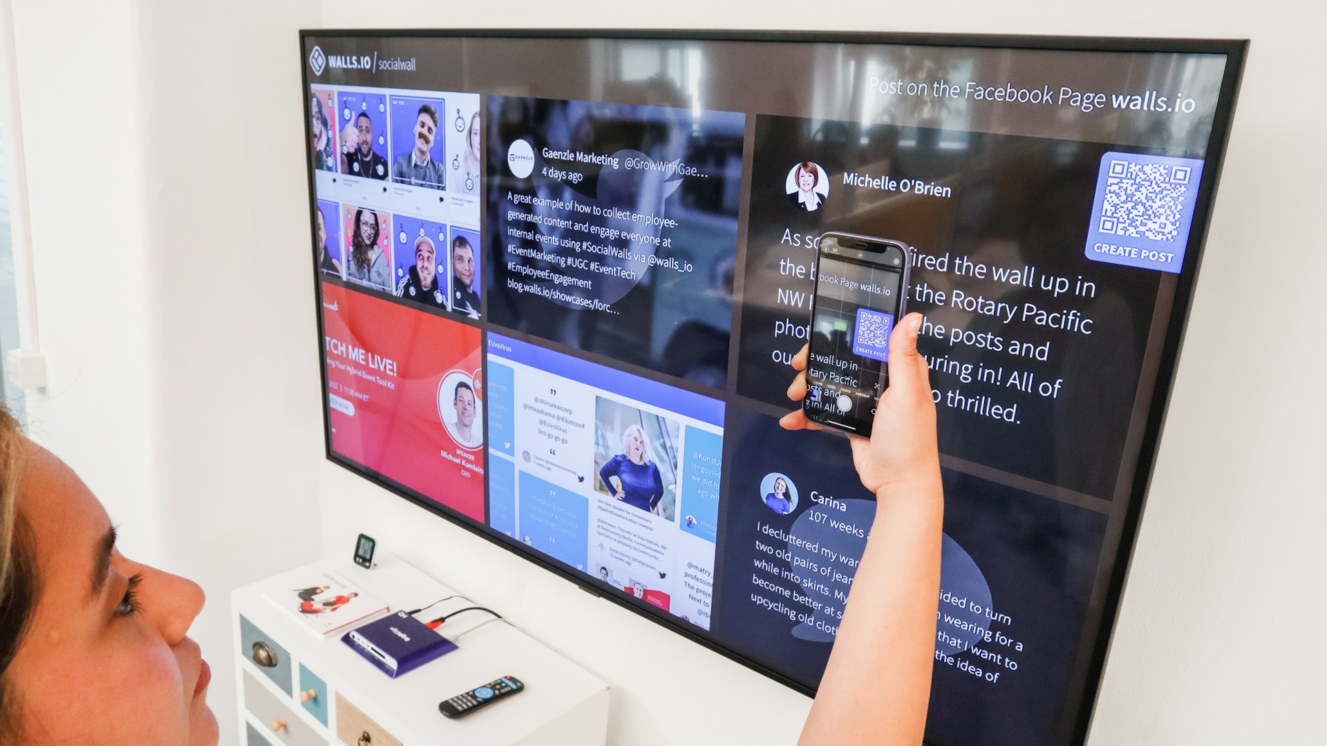 a woman holding a cell phone in front of a flat screen tv