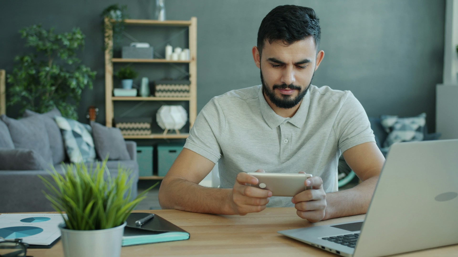 Man playing game on smartphone at desk with laptop